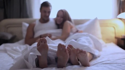 Couples feet sticking out from under duvet at home in bedroom Stockbeeldmateriaal 70985784