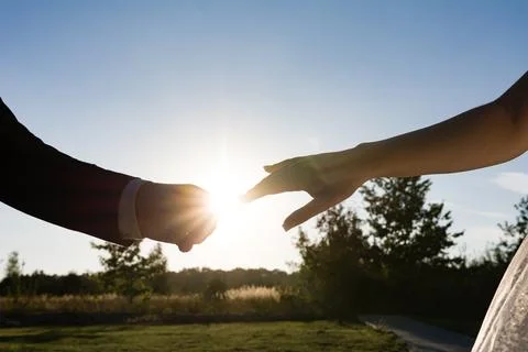 Couple's hands reaching towards each other, backlit by the setting sun. A s.. Fotos de archivo
