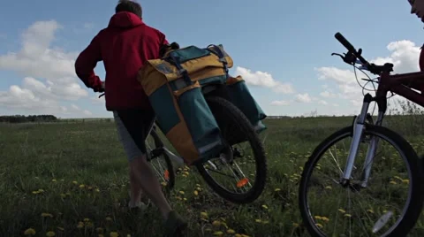 Couples with loaded bikes walks across a field Stock Footage 56979276
