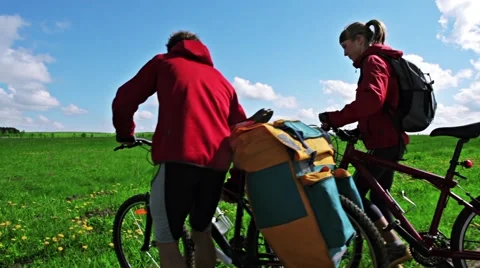 Couples with loaded bikes walks across a field Stock Footage 56980309