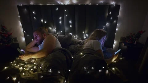 Couples spend cozy night in bed surrounded by Christmas lights and smartphones Stock Footage 307115274