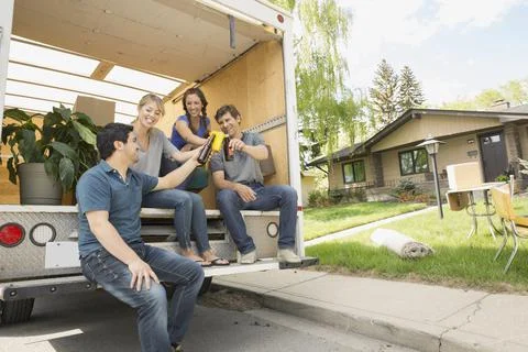 Couples toasting beer at back of moving van Stock Photos