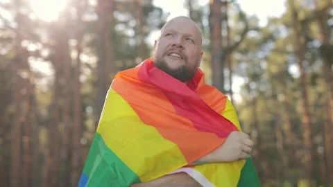 Courageous bold man with beard wrapped in a rainbow gay flag raise up it in sky Stock Footage 137325464