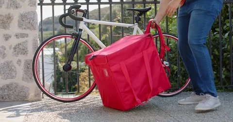 Courier approaching bicycle and bag on walkway, lifting bag onto back and Video stock 337294056