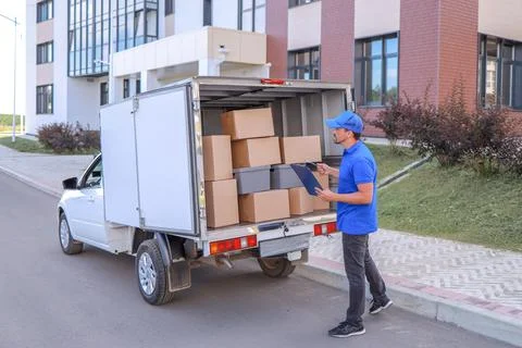 A courier in a baseball cap loads a van with boxes for delivery. concept Stock Photos
