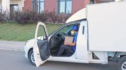 A courier in a blue uniform and a baseball cap gets out of a white van, delivery Stock Footage 315496181
