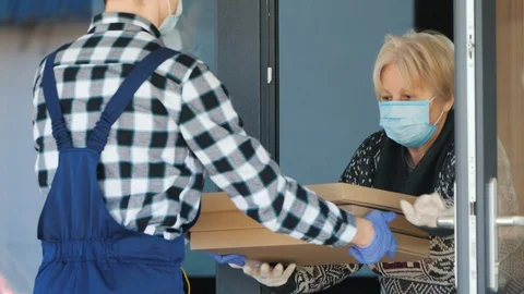 Courier brings pizza boxes to elderly woman. She wears a protective mask, picks Stock Footage 128224040