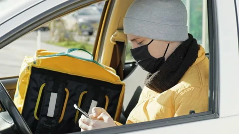 Courier in the car is on his phone, backpack for orders on the seat. Food Stock Footage 148651832