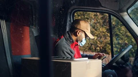 Courier checking map on the smartphone on drivers seat. Man with face mask Foto stock