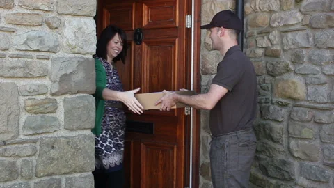Courier / Delivery man delivering a parcel home delivery at a house front door 스톡 동영상 134471328