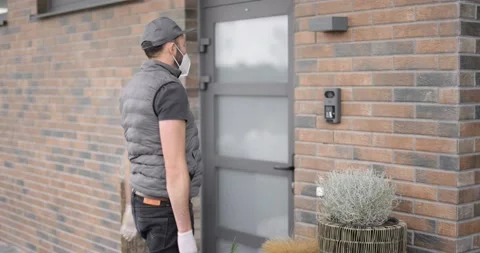 Courier in face mask delivers parcel for a young woman to home Stock Footage 154623481