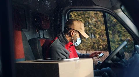 Courier getting in touch with client using smartphone on drivers seat. Man with Stock Photos