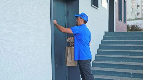 A courier knocks on a customers door to deliver an order with ready-made food in Stock Footage 316283526