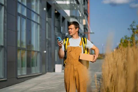 Courier man delivering packages, using smartphone for navigation and order Stock-Fotos