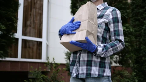 Courier man in protective mask and medical gloves delivers takeaway food Stock Footage 130813356