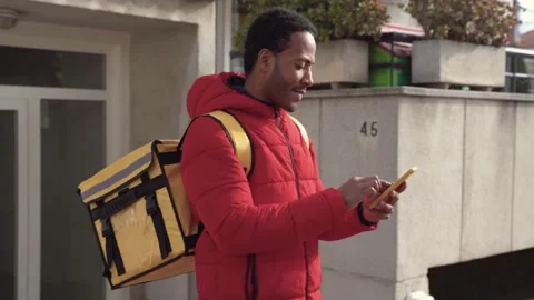 Courier man with yellow backpack searching address with mobile phone. Delivery Stock-Footage 228793873