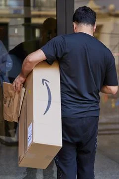 Courier with a parcel from Amazon is standing in front of the door of the hou Stock Photos
