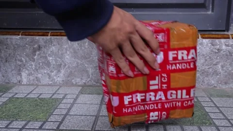 Courier places a parcel box with red label fragile on the floor 库存影片 275872396