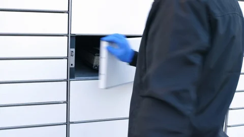 Courier in protective gloves inserting placing package in box in parcel locker Vídeo Stock 128879319