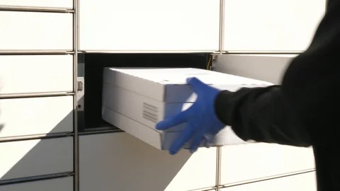 Courier in protective gloves inserting placing package in box in parcel locker Stock Footage 129100570