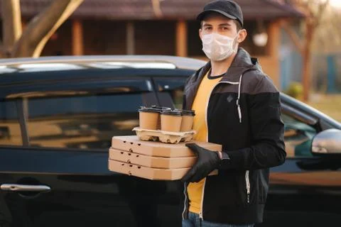Courier in protective mask and medical gloves take order from car. Delivery boy Stock Photos