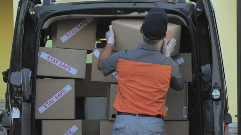 Courier with protective mask carrying package with stay safe label writing 스톡 동영상 137849867