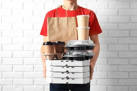Courier with stack of orders near white brick wall. Food delivery service 스톡 사진