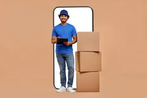 Courier with stack of parcels and clipboard near huge smartphone on dark be.. Stock Photos