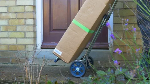 Courier wheeling a large parcel on a trolley to a house front door. Video stock 144095915