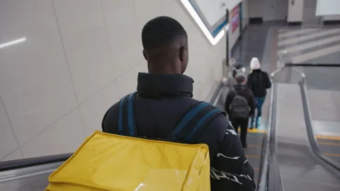 A courier with a yellow backpack descends on the escalator Stock Footage 279731239