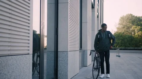 Courier with yellow backpack walks next to the bike and pulls out a mobile phone Stock Footage 254100131