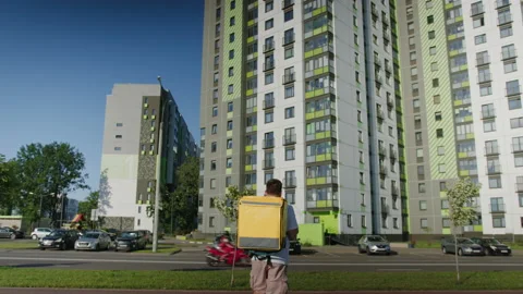 Courier with a yellow bag is walking down the street in search of the building Stock Footage 233979204