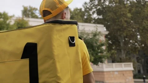 The courier in a yellow uniform adjusts a baseball cap Video stock 130660364