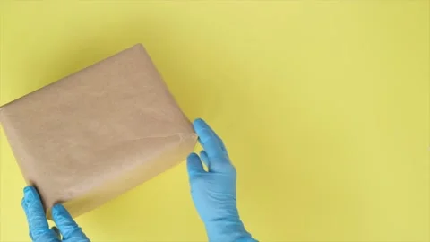 Courier's hands in protective gloves puts parcel on yellow background. 库存影片 130678494