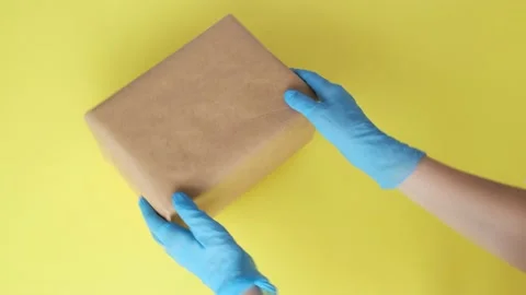 Courier's hands in protective gloves rotate parcel on yellow background. 스톡 동영상 130678721