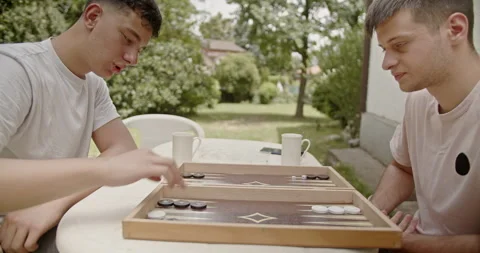 Cousins are seen playing backgammon on a sunny day in an outdoor setting Stock Footage 281965280