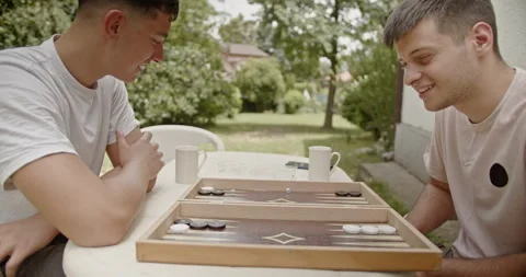 Cousins engaged in a game of backgammon outside, sharing a peaceful and Stock Footage 282323881