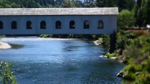 COVERED BRIDGE OVER BLUE RIVER AS LOGGING TRUCK DRIVES THROUGH SUN BRIGHT Stock Footage 80693668