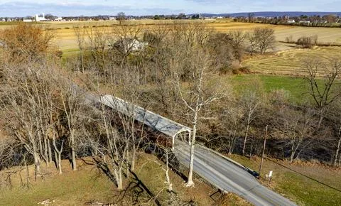 Covered Bridge Spans Tranquil Stream in Rural Landscape With Farms and Gree.. Stock Photos
