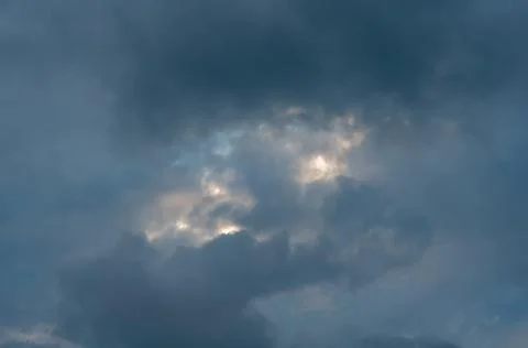 Covered with dark blue clouds with small gap through which sun's rays and bright Stock Photos