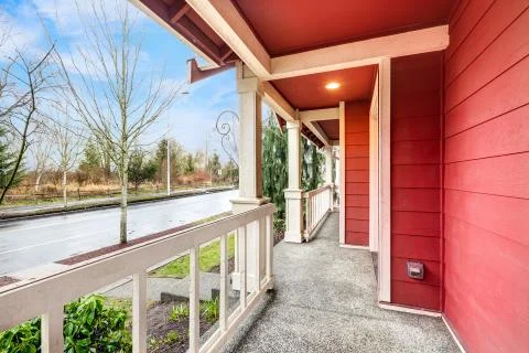 Covered front porch of red two story home with railings and square columns. N Stock Photos