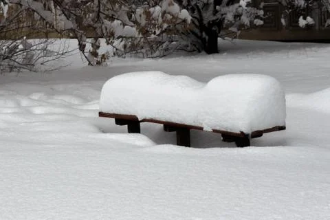 Covered with a large layer of snow bench in the city park Stock Photos