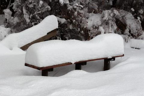 Covered with a large layer of snow bench in the city park Stock Photos