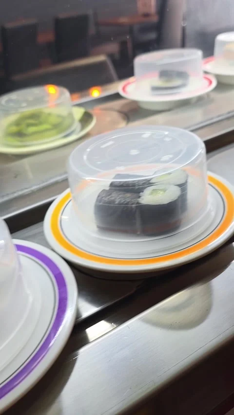 Covered sushi plates move along a rotating conveyor belt in a Japanese rest.. Video stock 340926333