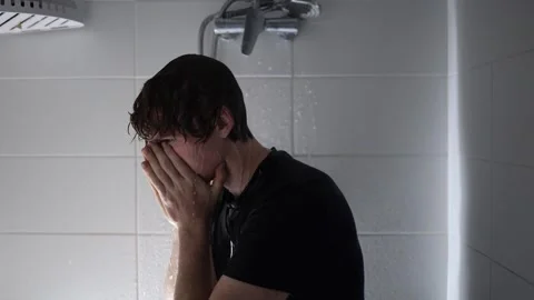 Covers his face with both hands under the shower water a student in wet black sh Stock Footage 315991725