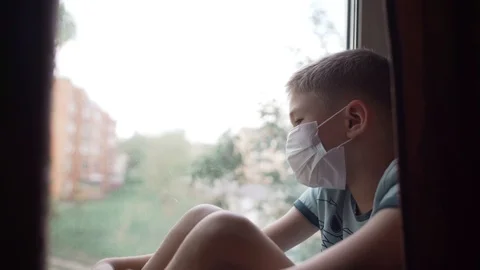 Covid -19, a boy sitting by the window in a medical mask, coronavirus pandemic Stock Footage 130137583