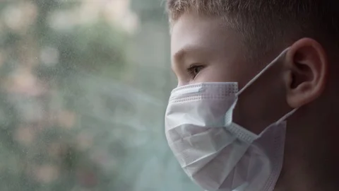 Covid -19, a boy sitting by the window in a medical mask, coronavirus pandemic Stock Footage 130137733