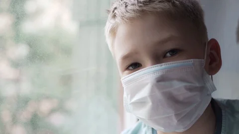 Covid -19, a boy sitting by the window in a medical mask, coronavirus pandemic Stock Footage 130137854