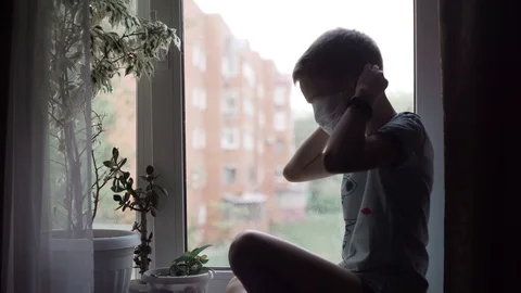 Covid -19, a boy sitting by the window in a medical mask, coronavirus pandemic Stock Footage 130137900