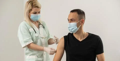 COVID-19 vaccine injection, doctor in gloves holds syringe and makes jab to Stock Photos